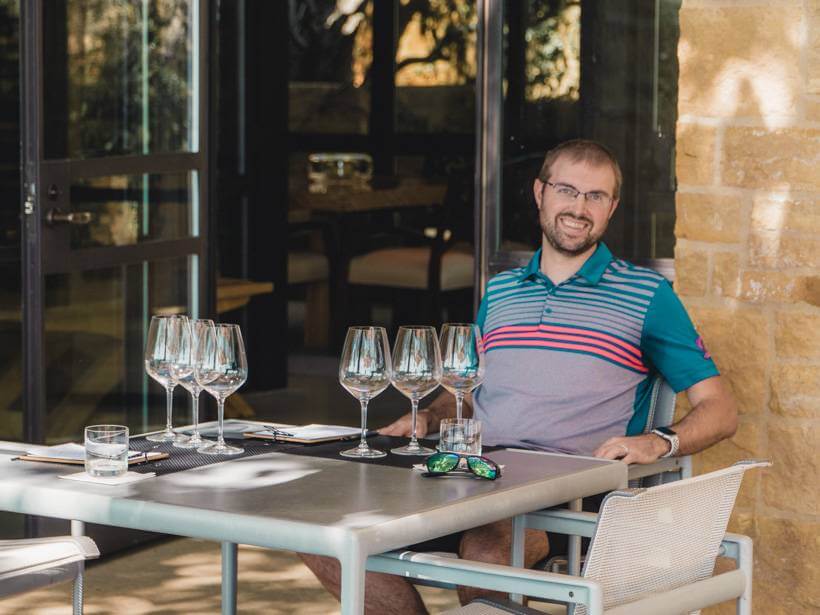 Man sitting on terrace of stone tasting room at O'Shaughnessy Estate Winery with empty wine glasses on table - wineries to visit in napa valley