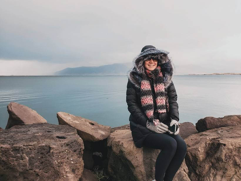 Girl in black down coat and knit scarf sitting along the sea in Reykjavik- 4 days in Iceland