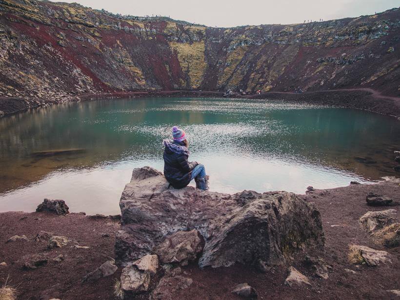 girl sitting on bench before turquoise lake in kerid crater