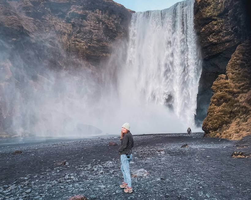 Girl in light green hat and black fleece standing in front of Skogafoss waterfall at dusk - 4 days in Iceland