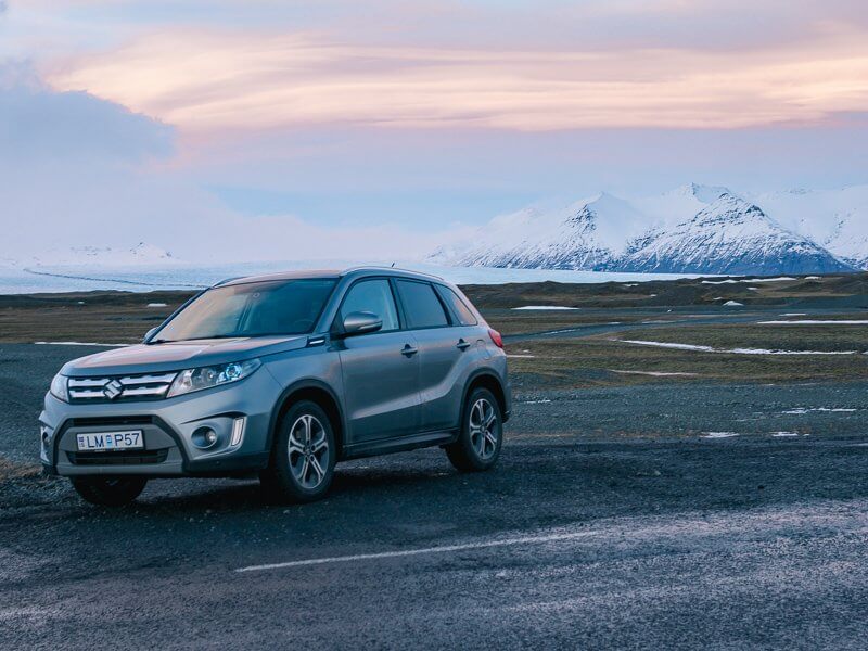 Small SUV on side of empty Iceland road with white mountains in the background