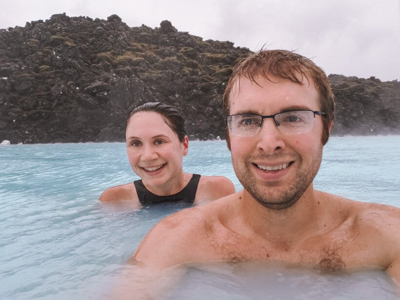 Couple soaking in milky Blue Lagoon waters in front of black volcanic rock