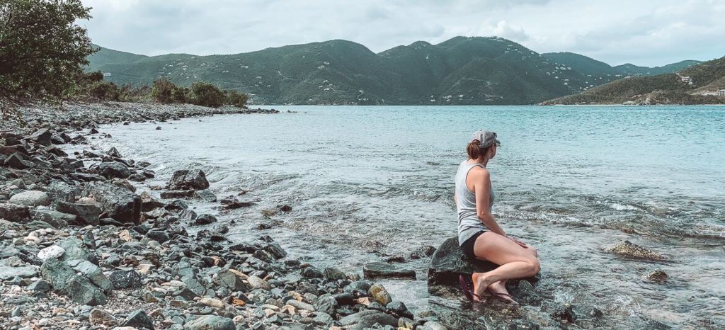 girl sitting on rocky beach looking out into a Caribbean Bay