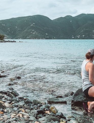 girl sitting on rocky beach looking out into a Caribbean Bay