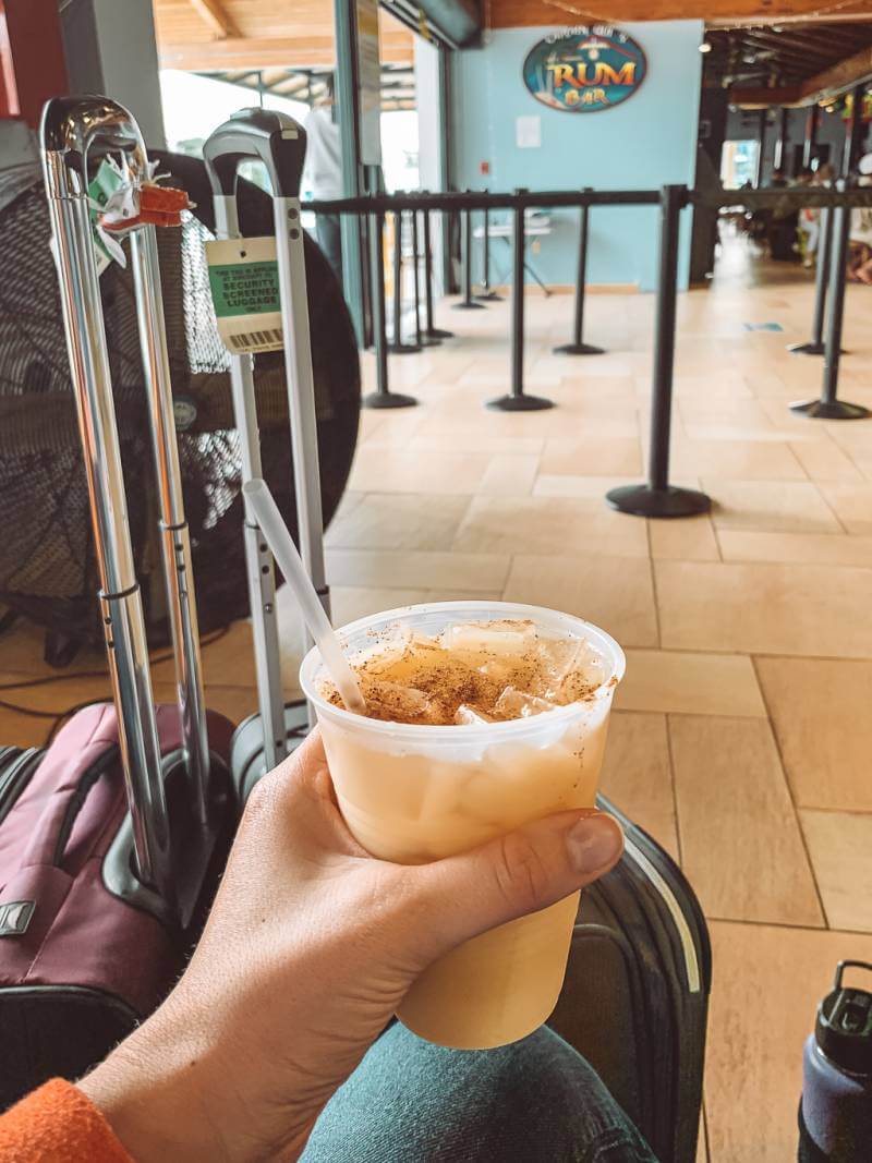 girl holding tropical drink with suitcases waiting for ferry - caribbean packing list