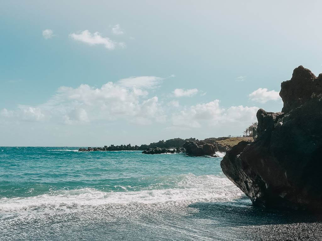 blue ocean of the black sand beach on road to hana in maui