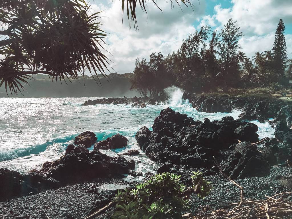 wild blue waves crashing against black volcanic road along road to hana