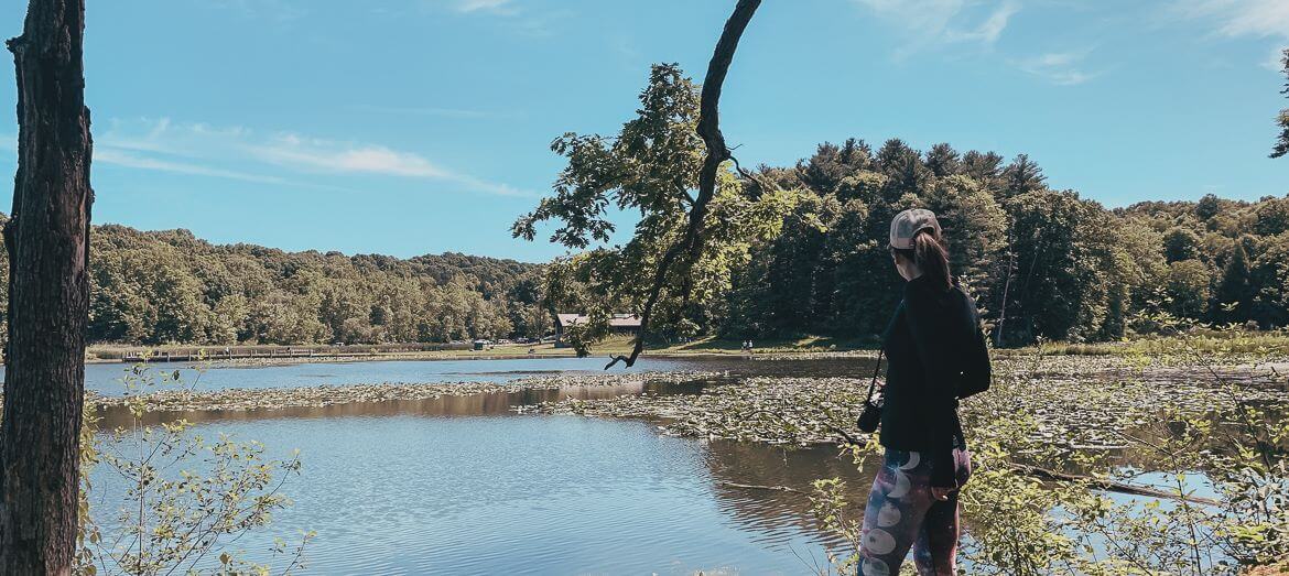 girl standing in front of blue lake surrounded by woods