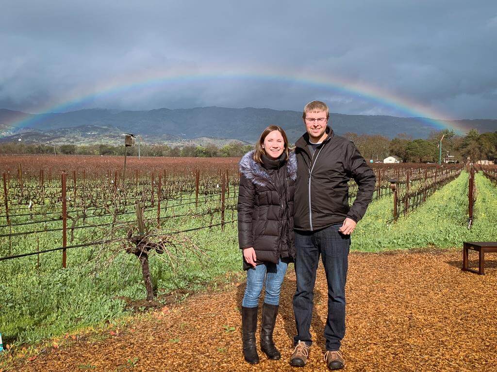 Couple standing in front of Biale vineyard with rainbow in the background