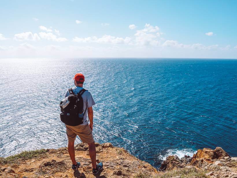 man standing atop ram head before blue ocean on ram head trail