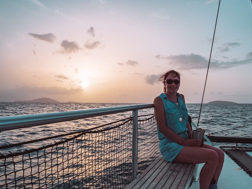 girl sitting towards front of catamaran in blue romper during sunset