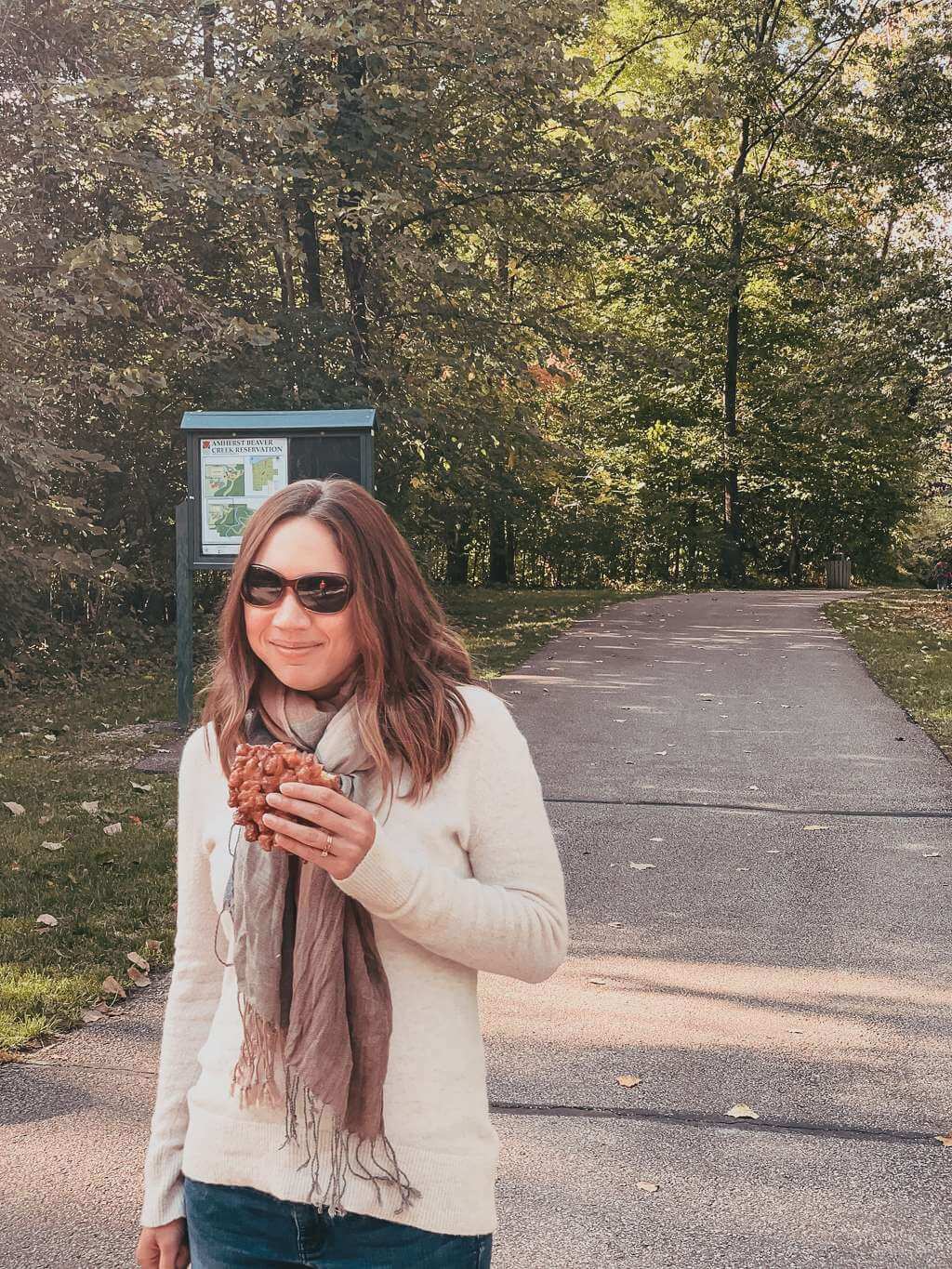 girl holding apple fritter on wooded path in amherst ohio