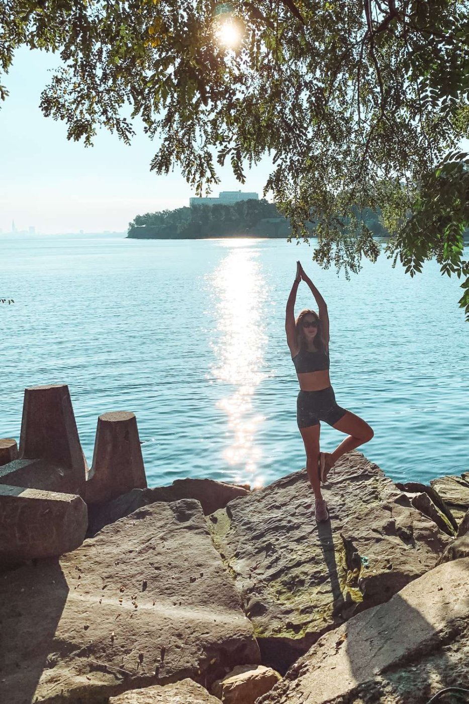 brunette girl in black yoga clothes doing tree pose near a lake