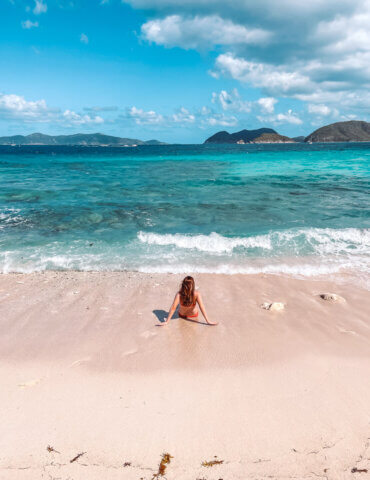 Girl sitting in sand at Denis Bay letting waves wash over legs - best st john usvi beaches