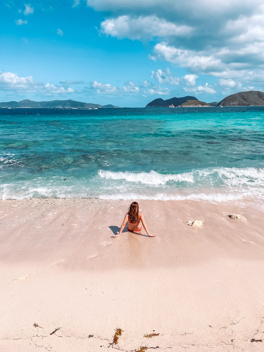 Girl sitting in sand at Denis Bay letting waves wash over legs - best st john usvi beaches