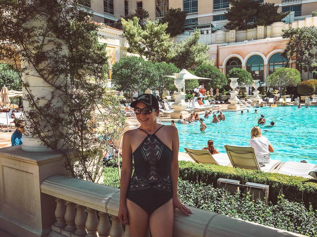 Girl standing in front of Bellagio pool in blue one piece swimsuit