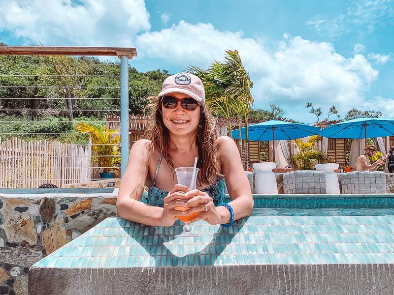 Girl in baseball cap with drink in infinity pool during first solo trip