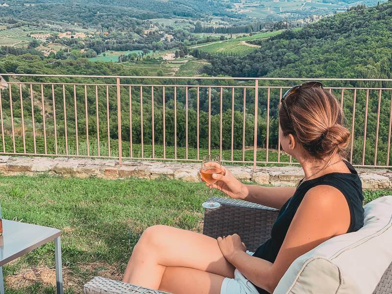 Brunette girl in black tank top sipping rose while admiring rolling hills of Tuscany