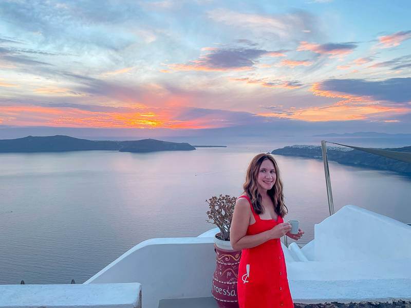 brunette girl in red dress sipping espresso in Santorini in front of Caldera at sunset