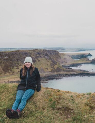 Girl sitting on Giant's Causeway with cliffs in the background - 2022 goals spring update