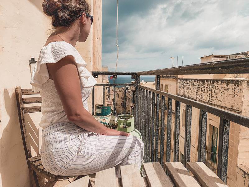 Girl sitting on balcony of Airbnb looking towards Mediterranean - solo travel Malta