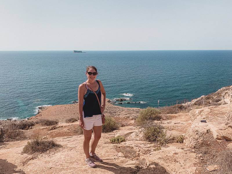 Girl standing in front of Mediterranean in dry brown earth - solo travel Malta