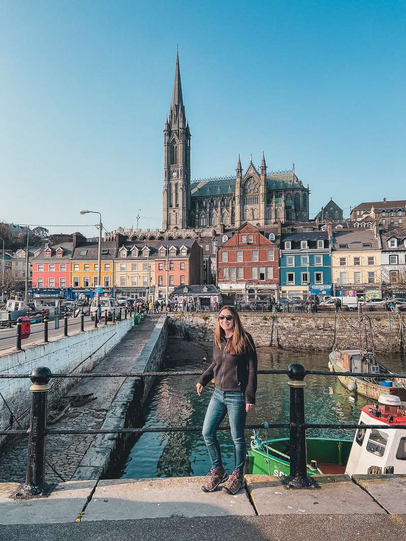 Brunette girl in black fleece standing in front of colorful harbor in Cobh
