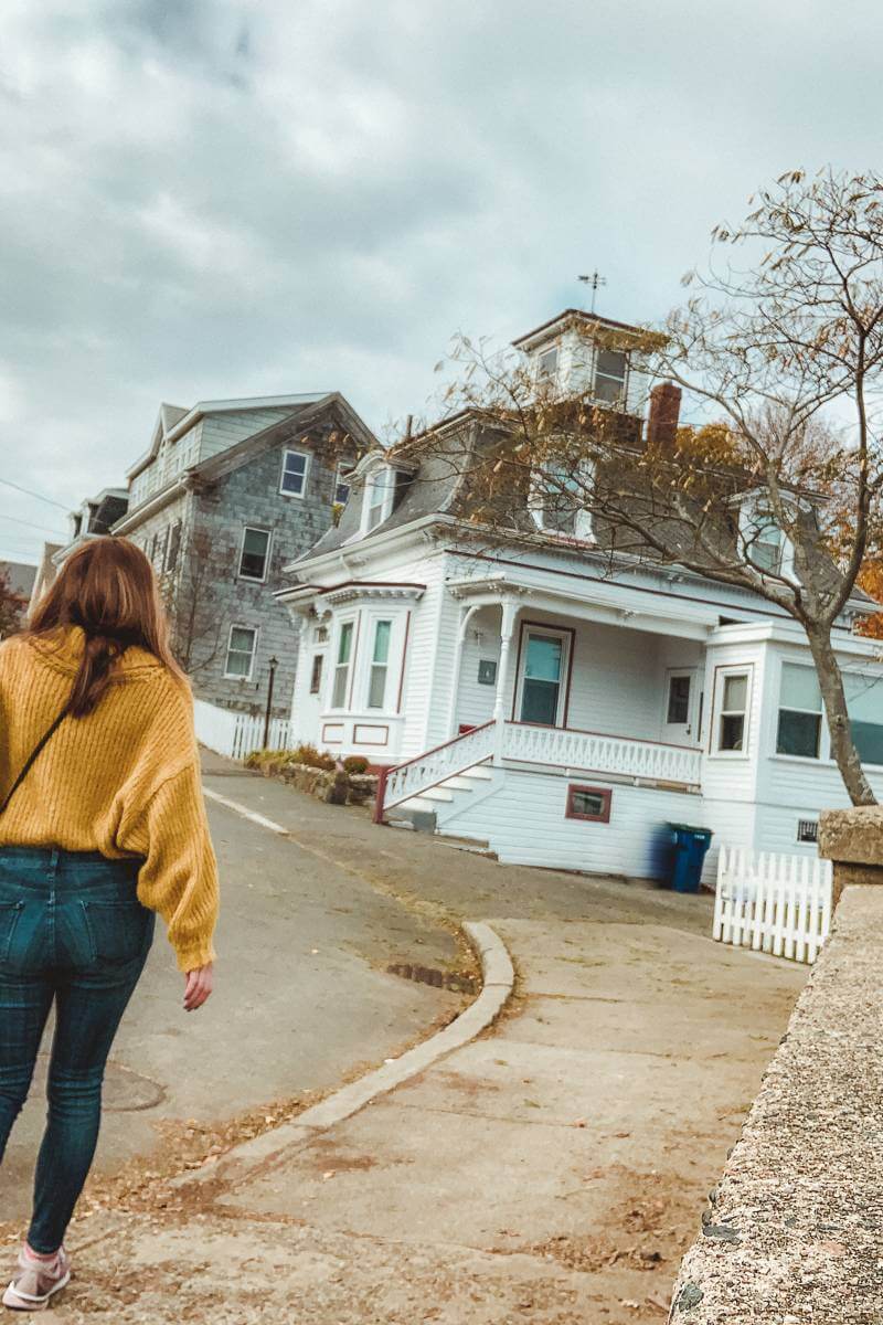 Girl walking towards Hocus Pocus House in yellow orange sweater- trip to Salem MA