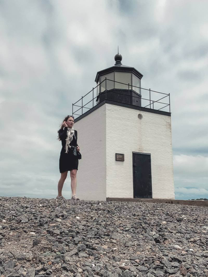 Girl in black dress and scarf walking past Derby Point Lighthouse