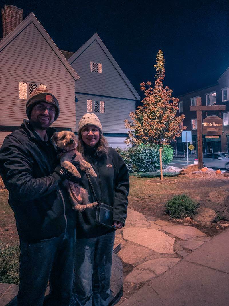 Couple with small dog standing outside Witch House at night