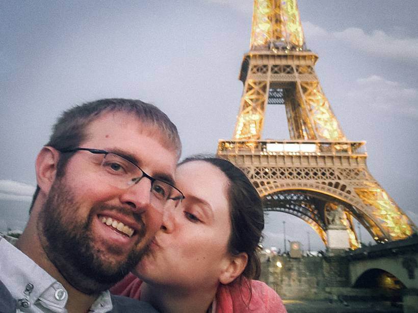 Woman kissing man on cheek while passing lit up Eiffel Tower on Bateaux Mouches