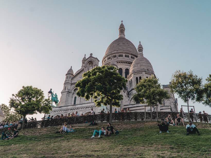 View from bottom of grassy hill up at white facade of Sacre Coeur