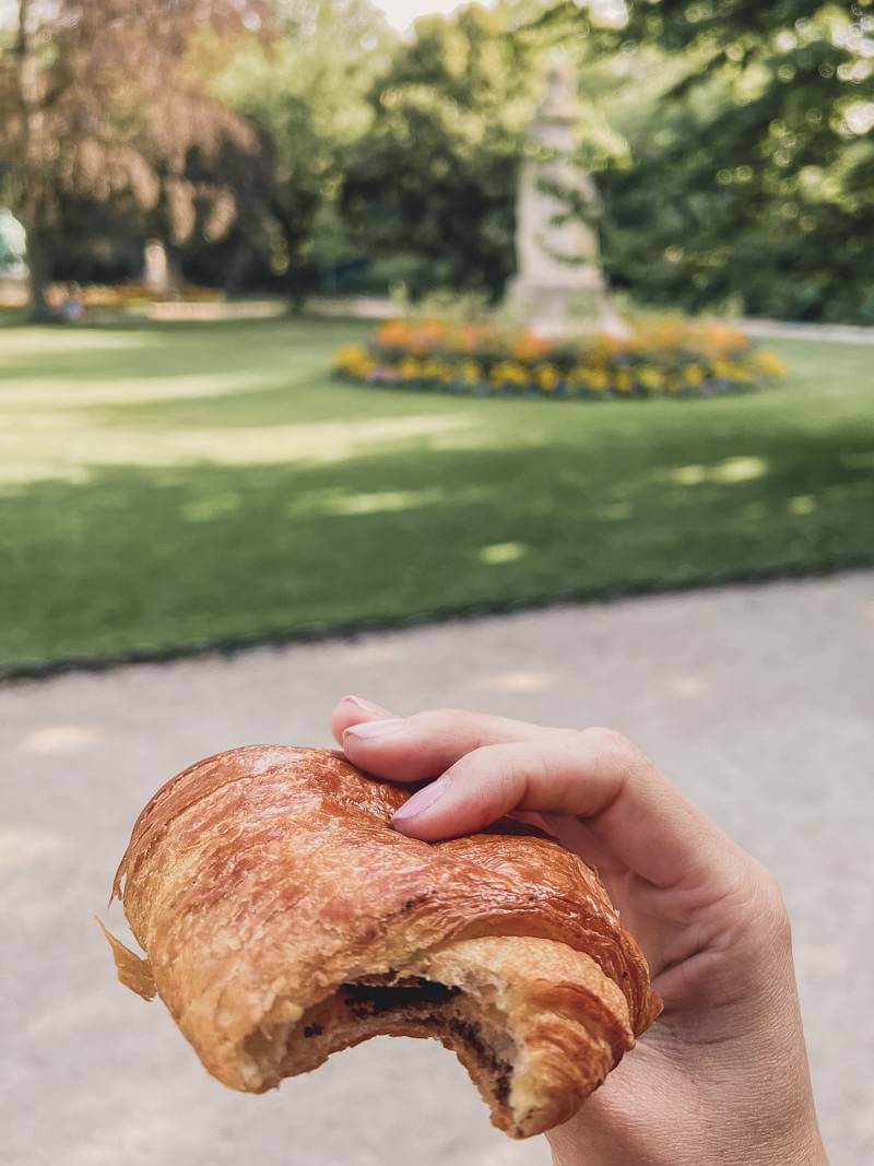 Holding a pain au chocolat at Luxembourg Gardens in Paris