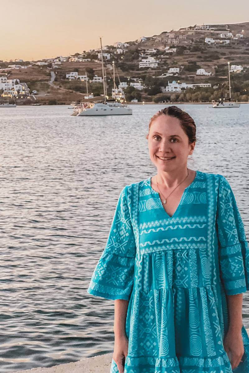 Girl in blue linen embroidered dress standing near harbor in Parikia, Paros