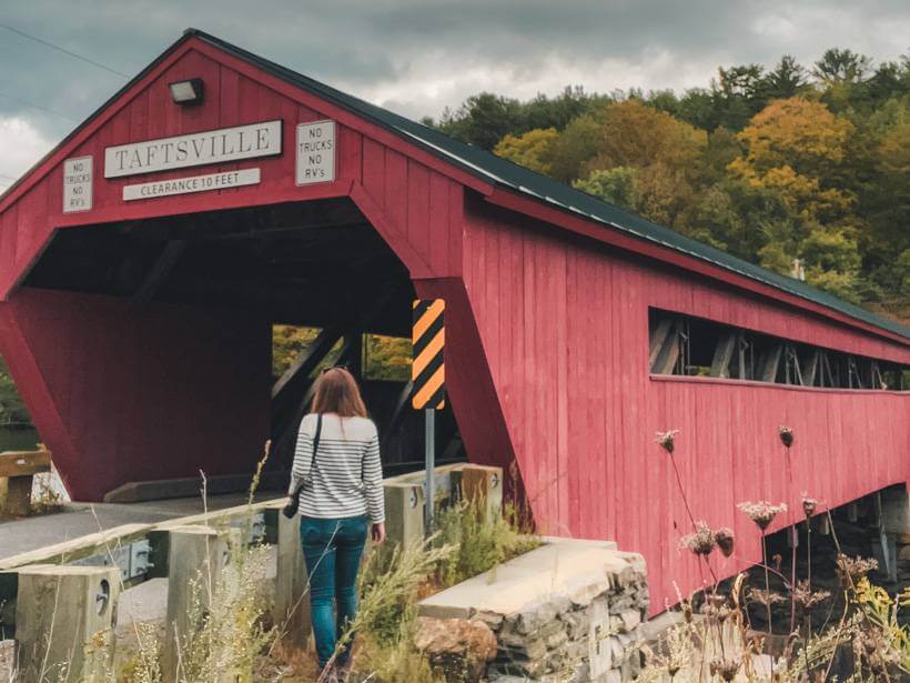 Girl standing by red covered bridge in Vermont
