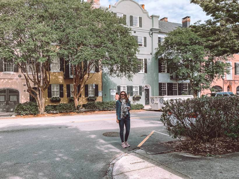 Girl in jeans and denim button up in front of colorful pastel rainbow row in Charleston SC during road trip to Savannah GA