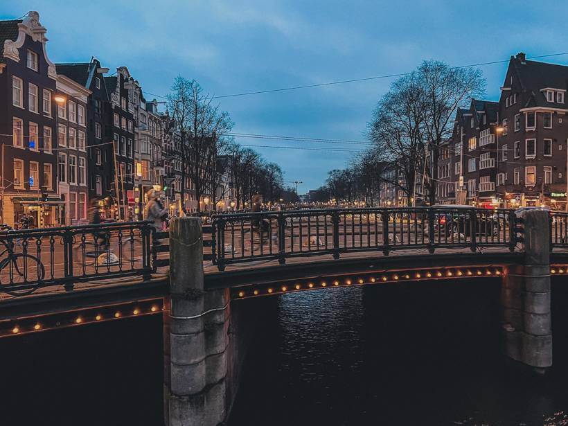 One of Amsterdam's canal bridges at night, as bikers cross it - solo travel Amsterdam