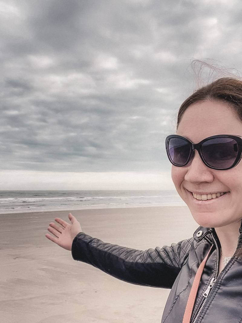 Girl in faux leather jacket taking selfie while strolling down Folly Beach - solo trip to Charleston, SC