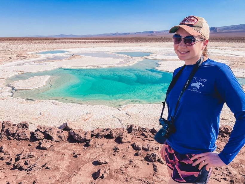 Girl in blue sunshirt and baseball cap standing in front of bright aqua Laguna Baltinache - Chile packing list