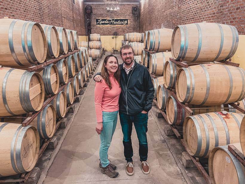 Woman in pink shirt and man in black windbreaker posing in between wine barrels at a winery