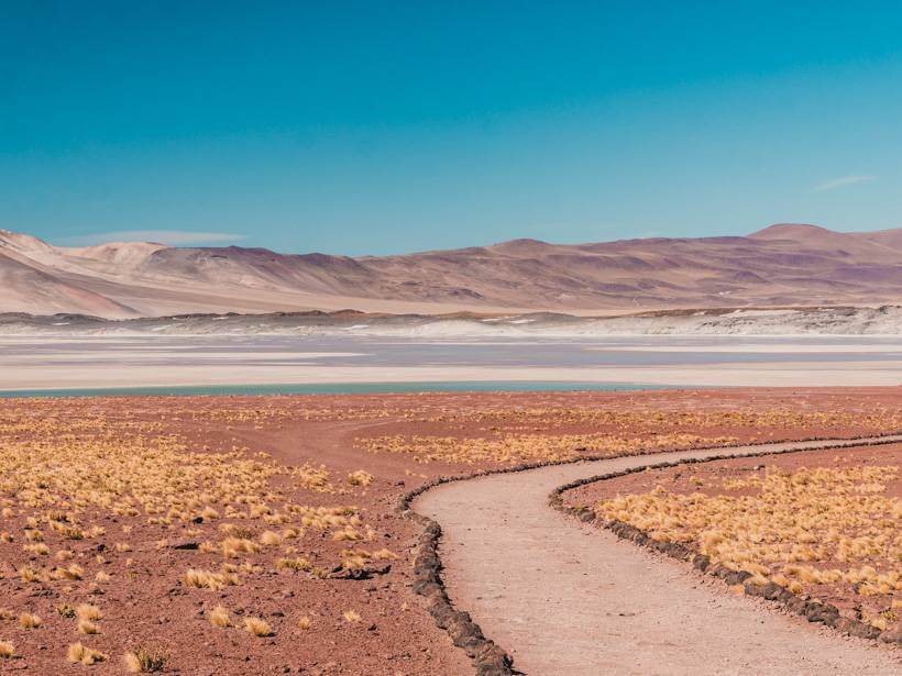 Reddish terrain leading to sky blue water - Atacama Desert itinerary