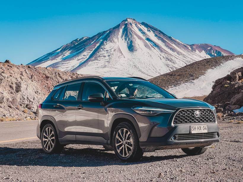 Small SUV parked on a pull-off in the Atacama Desert with a snow-capped mountain directly behind it