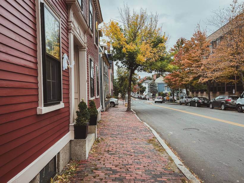 Old house with red siding along brick sidewalk with colorful fall trees in Salem, MA