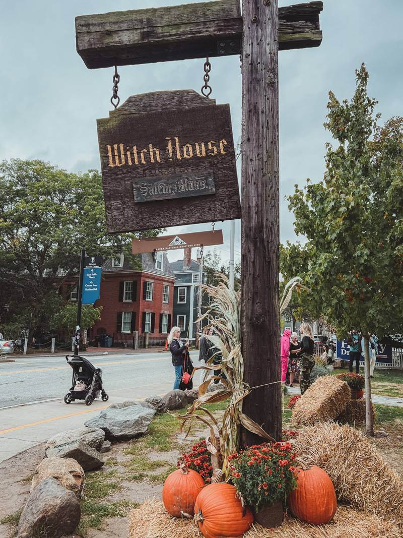 Wooden hanging sign for The Witch House decorated with pumpkins and hay bales in October