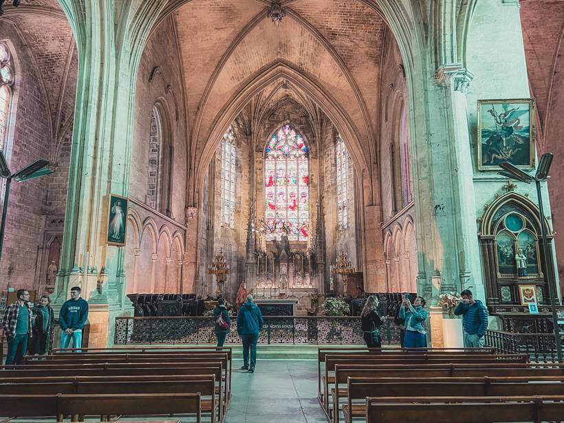 Stone interior and wooden church pews leading to stained glass windows behind alter of Collegiate Church of Saint-Emilion