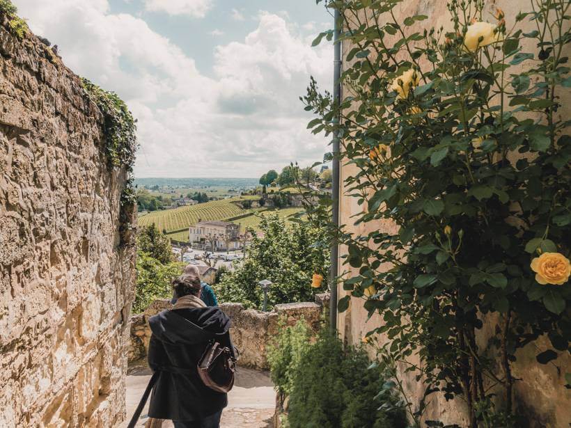 Couple wandering down stone path passed stone walls and yellow flowering bush with countryside views in the background