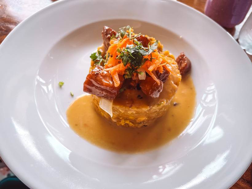 White plate with a yellow mofongo shell with sauce and meat