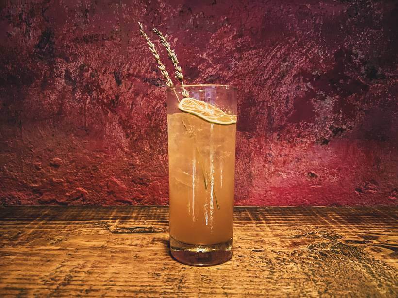 Tropical cocktail in a tumbler in front of a red wall at La Factoria