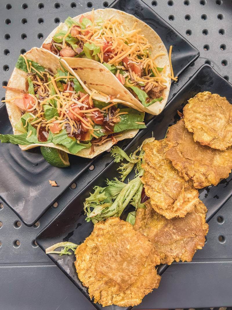 Tacos and tostones on black trays and a black table